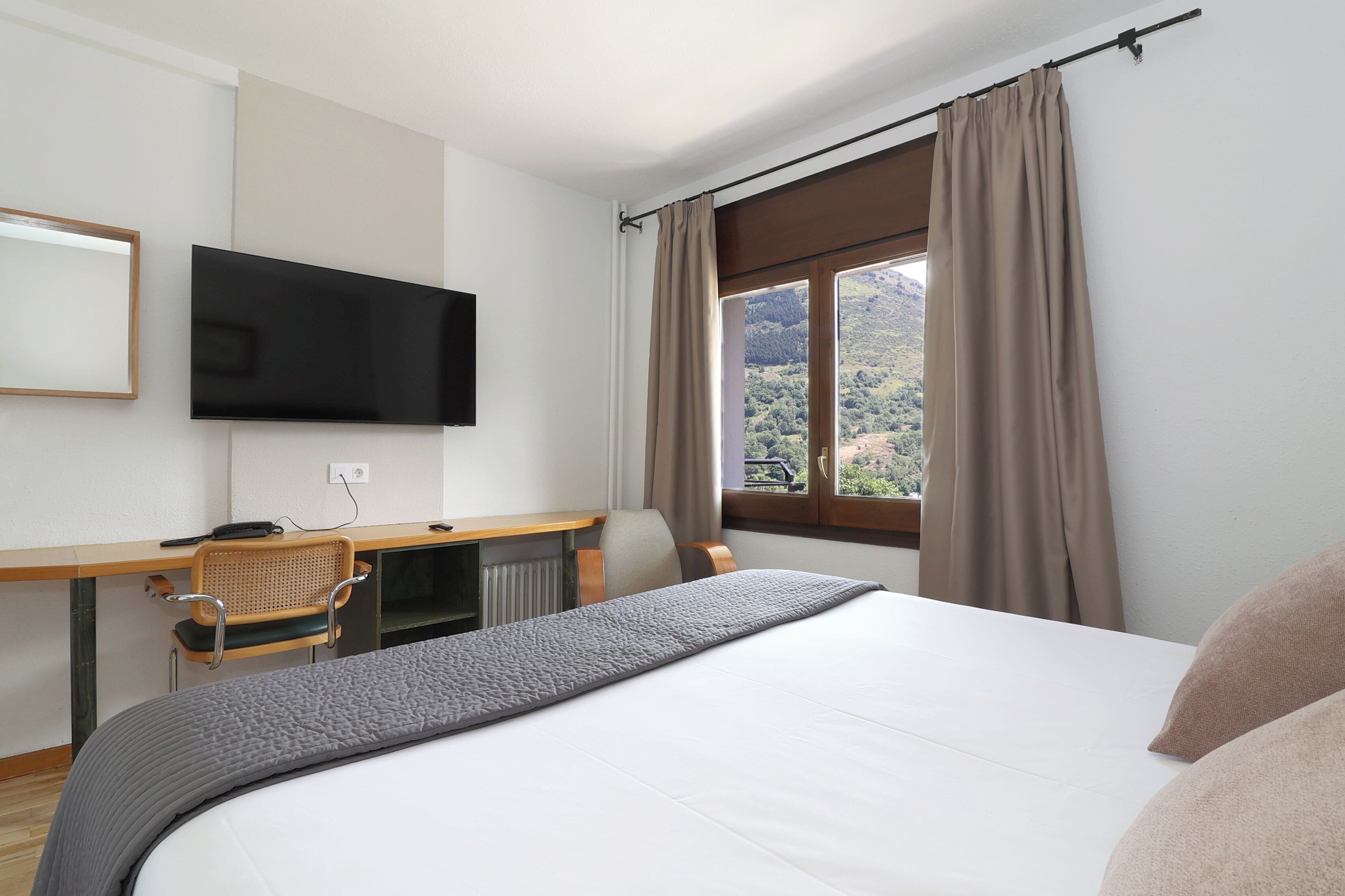 Una habitación de hotel con cama, escritorio con silla, televisión y ventana con cortinas.