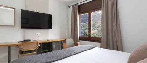 A hotel room with a bed, a desk with a chair, a television, and a window with curtains.