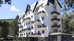 Un hotel de varios pisos con balcones, un restaurante y vistas del bosque circundante.