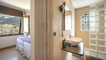 Une chambre avec une grande fenêtre, une salle de bain avec un lavabo et un miroir, et une vue sur les montagnes.
