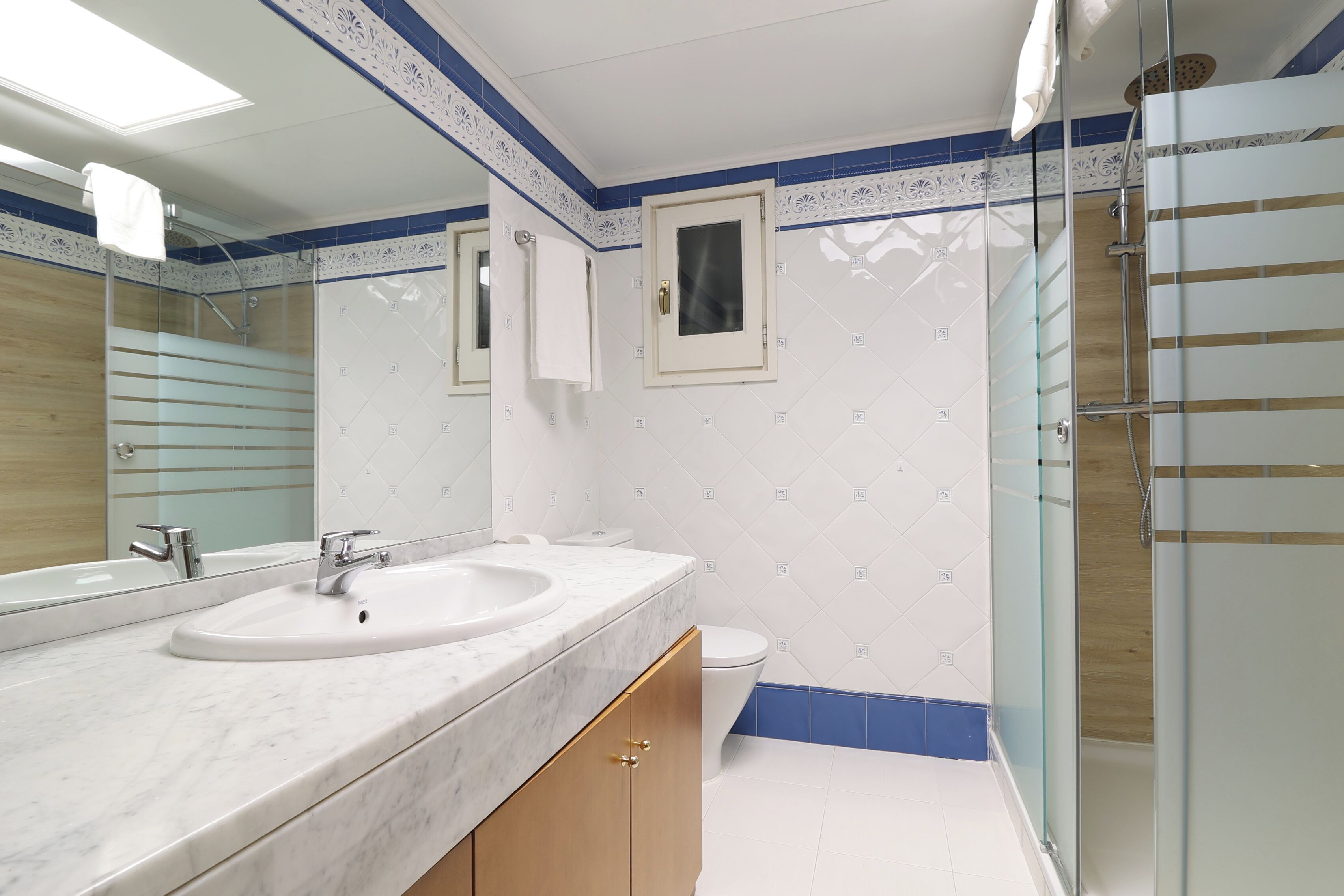Un baño con un espejo grande, dos lavamanos, un inodoro y una zona de ducha.