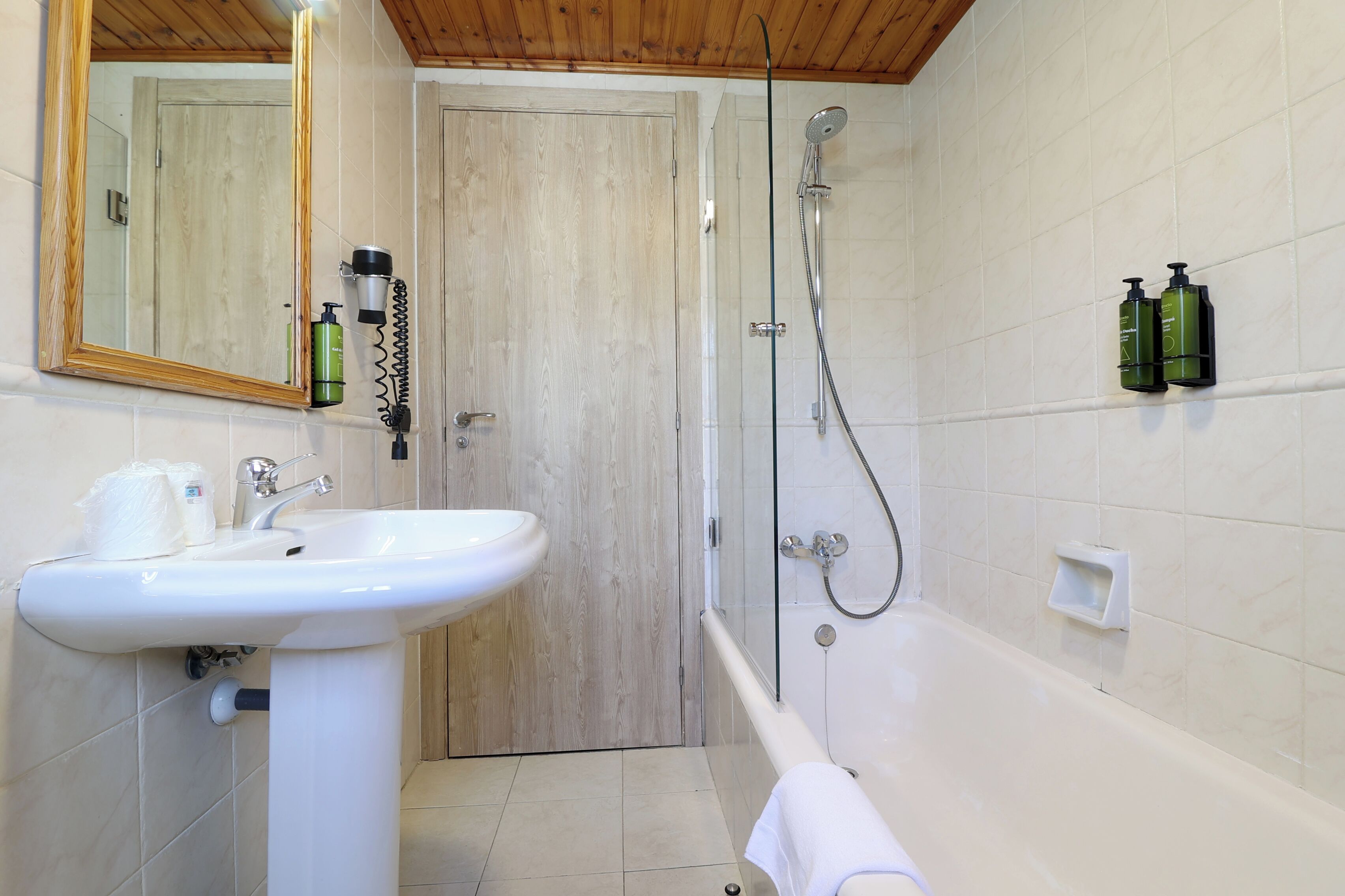 Un baño con un lavamanos blanco, un espejo, una ducha y dos botellas verdes en la pared.