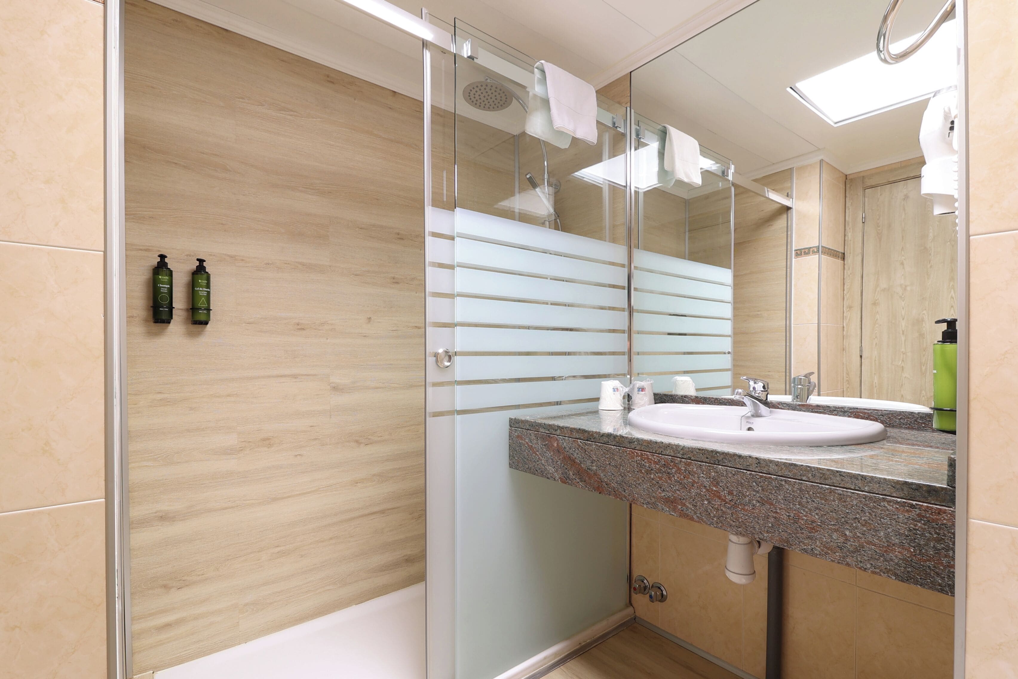 A modern bathroom with a glass shower enclosure, a granite countertop sink, and a large mirror.