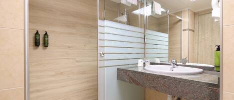 Un baño moderno con cabina de ducha de vidrio, lavabo con encimera de granito y un espejo grande.