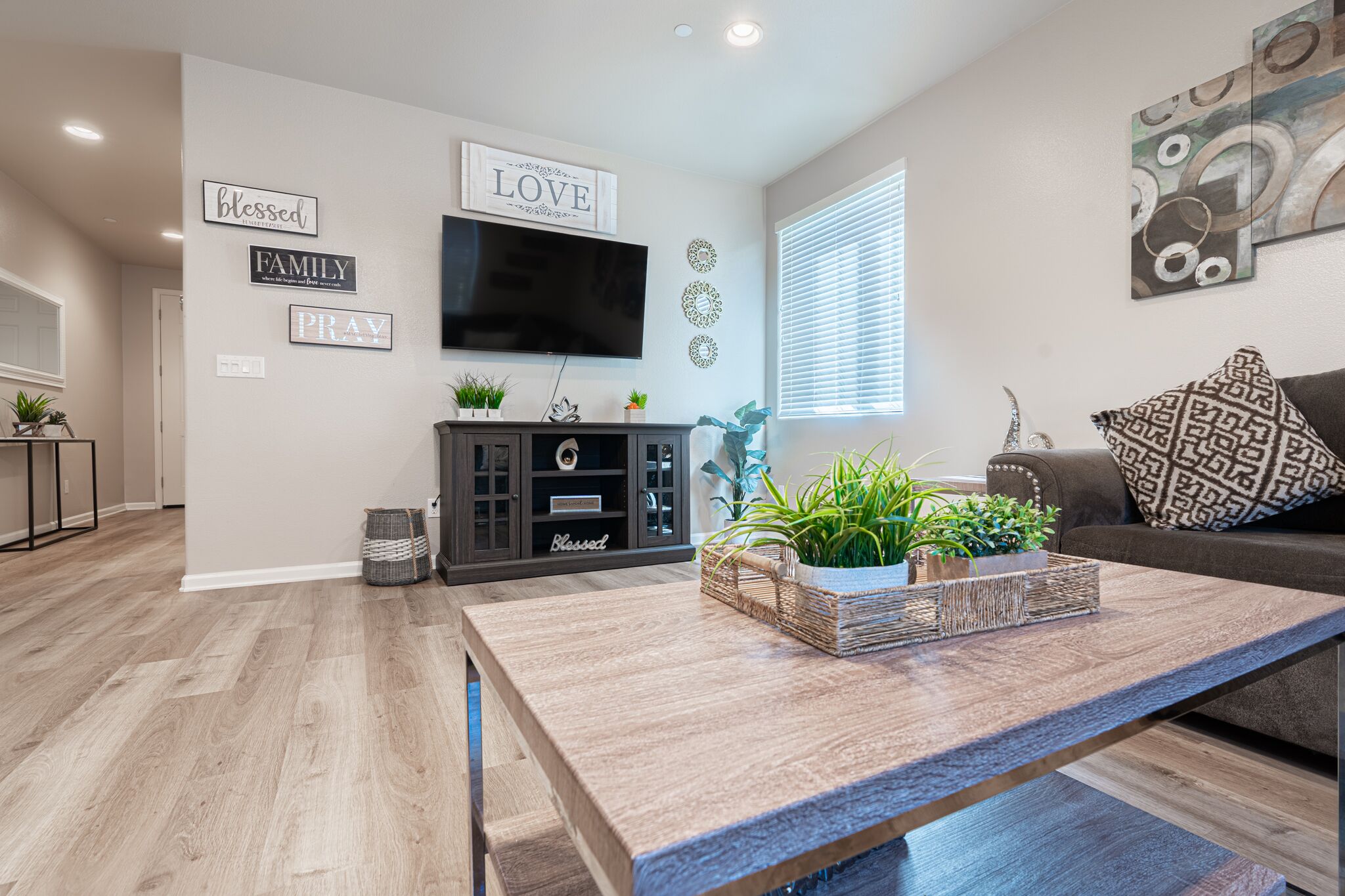 Una sala de estar moderna con un televisor de pantalla plana, una mesa de centro con plantas, un sofá gris y decoración en la pared.