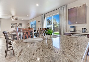 A modern kitchen with granite countertops, a dining area with a round table and chairs, and a view of the outdoors through large windows. - Cozy 6-Bedroom home perfect for large groups (Fresno)