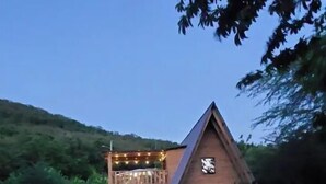 A modern house with a triangular roof, a balcony with string lights, and a garden with outdoor lighting.