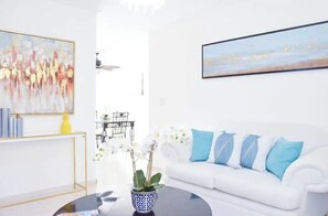 Un salon moderne avec un canapé blanc, des coussins bleus, une table basse et des œuvres d’art accrochées aux murs.