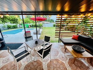 An outdoor patio area with a pool, a table with chairs, a sofa, and a wooden pergola with string lights. - Modern Vacation Home with pool- Conveniently located to Restaurants & Beach (North Miami)