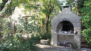 Forn de pedra a l'aire lliure en una zona boscosa, amb un ambient rústic.