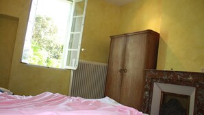 Un dormitori amb un llit, un armari de fusta, un radiador i una finestra amb vista a arbres.