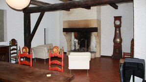 Habitació amb bigues de fusta a la vista, una llar de foc, un rellotge i un sofà blanc.