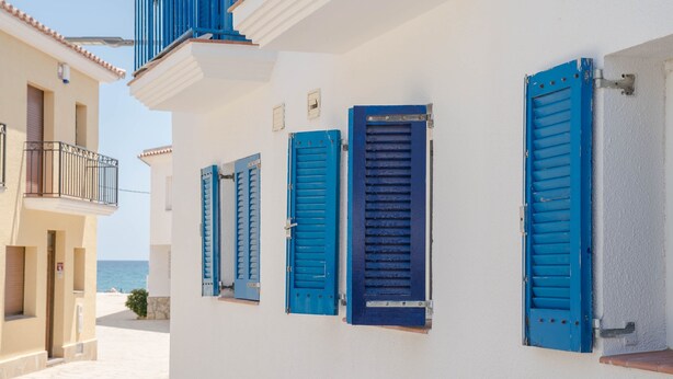 Un edificio costero con contraventanas azules y un balcón.