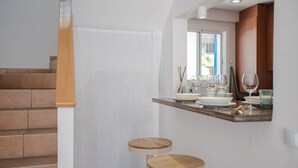 Una cocina con una escalera de madera, una cortina blanca y una zona de bar con taburetes y vasos.
