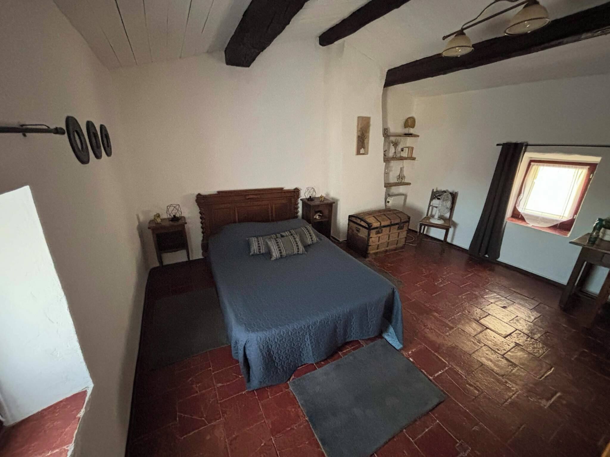 Un dormitorio con cama, cómoda, mesita, ventana y estante en la pared.