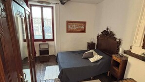 Un dormitorio con cama de madera, una mesita de noche, un aparador y una ventana con vistas a edificios.