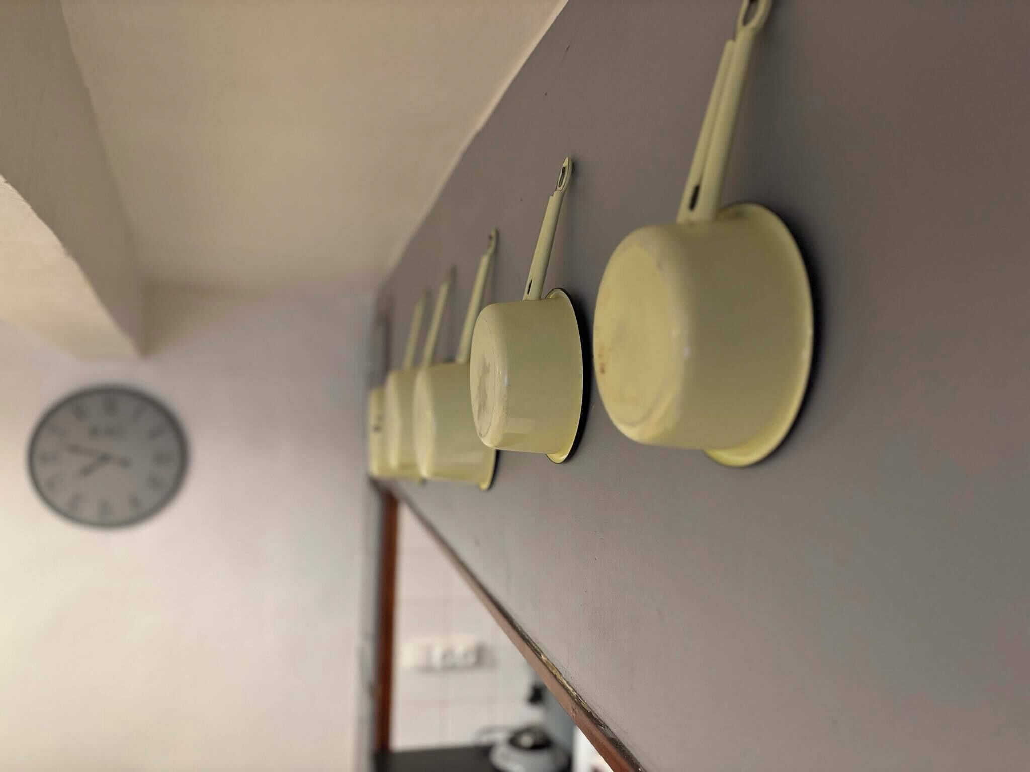A kitchen with a clock on the wall and a row of hanging pots.