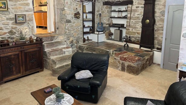 Una sala de estar acogedora con una pared de piedra, un sofá de cuero negro, una mesa de centro de madera y una araña.