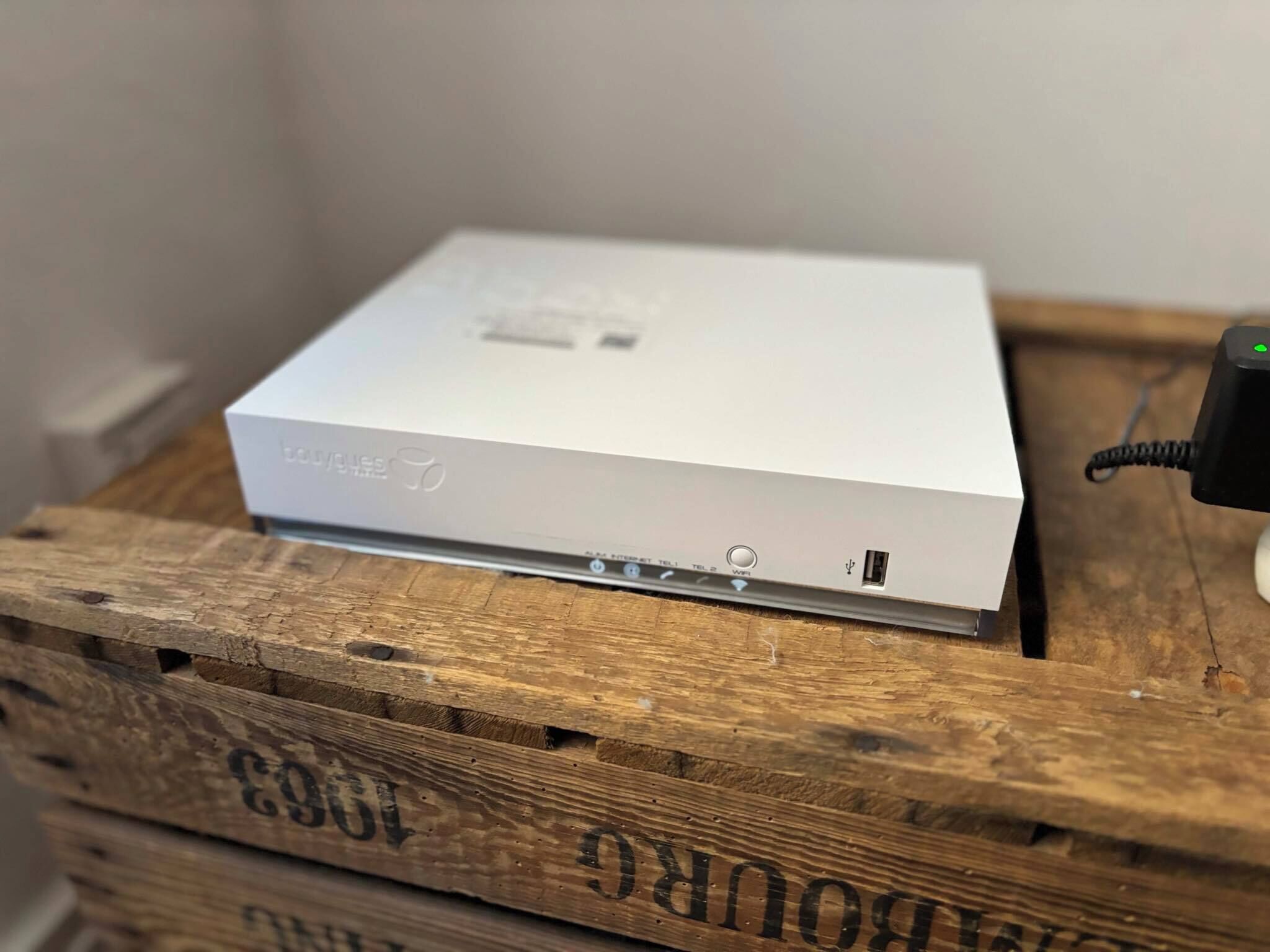 Un appareil électronique blanc, posé sur une caisse en bois, avec des ports visibles et un câble d’alimentation.