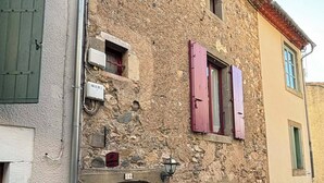 Un edificio de piedra con puerta de madera, una ventana pequeña con contraventanas y un letrero sobre la puerta.