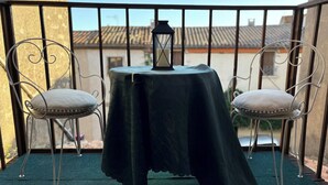 Un balcón con una mesa cubierta por un paño oscuro, dos sillas con cojines y un farol en la mesa.