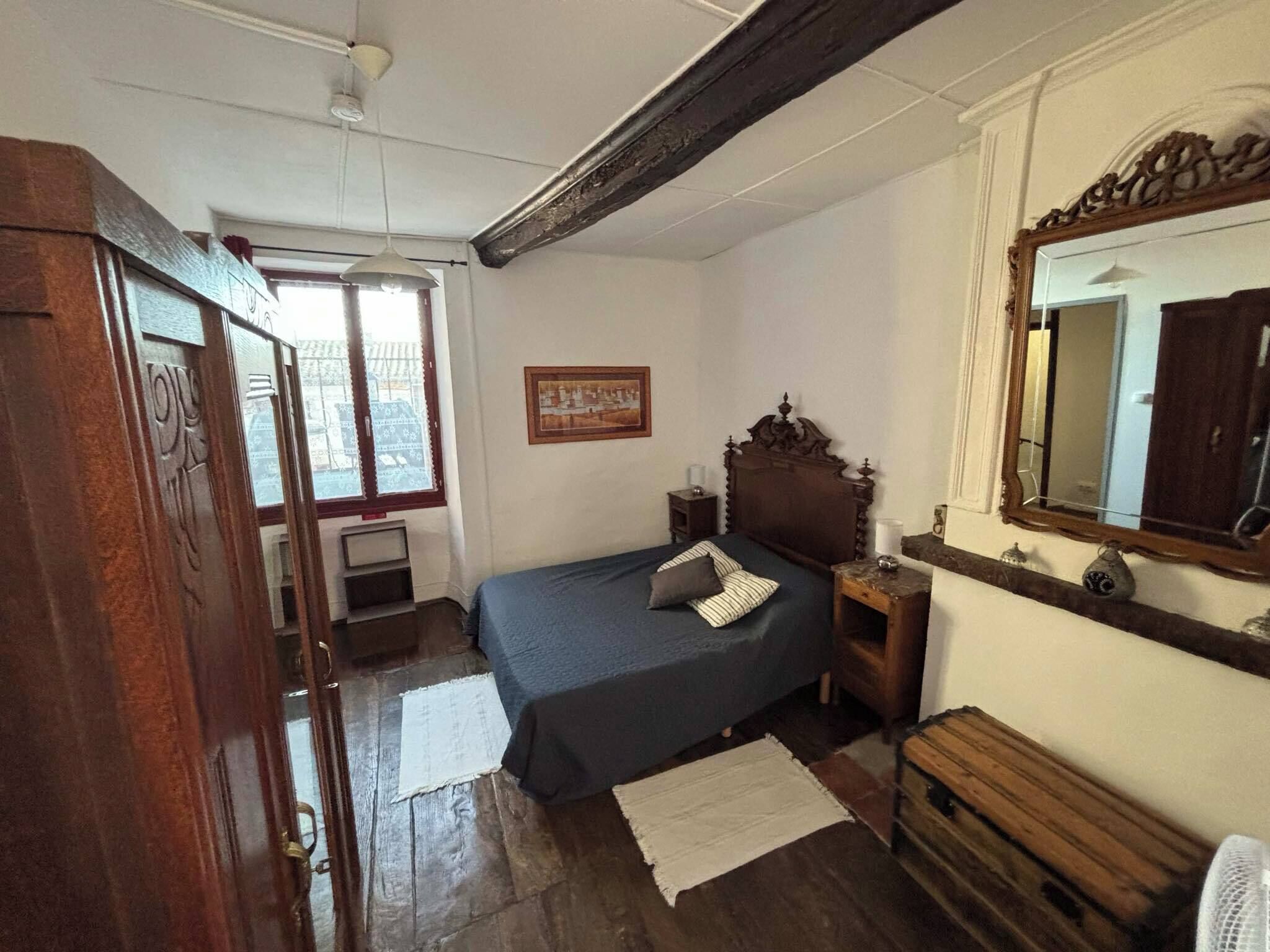 Una camera da letto con un letto di legno, un comodino, una cassettiera, uno specchio e una finestra con vista sugli edifici.