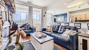 A spacious living room with a blue leather sofa, a coffee table, and a stone wall with a mounted animal head. - Pet Friendly, Spacious Home, Incredible Views, Private Hot tub 152 (Silverthorne)