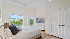Quarto com cama, penteadeira, televisão e uma janela grande com vista.