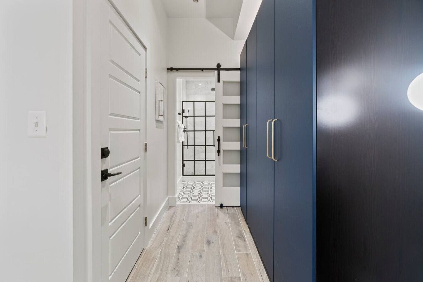 Un couloir avec des portes blanches, une armoire bleu foncé et un sol carrelé.
