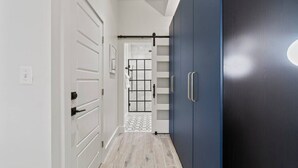 Um corredor com portas brancas, um guarda-roupa azul escuro e chão de azulejos.