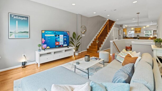 Uma sala de estar moderna com uma televisão de tela plana grande, uma escada e uma cozinha ao fundo.