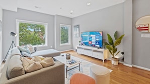 Uma sala de estar moderna com uma televisão grande, assentos confortáveis e janelas amplas.