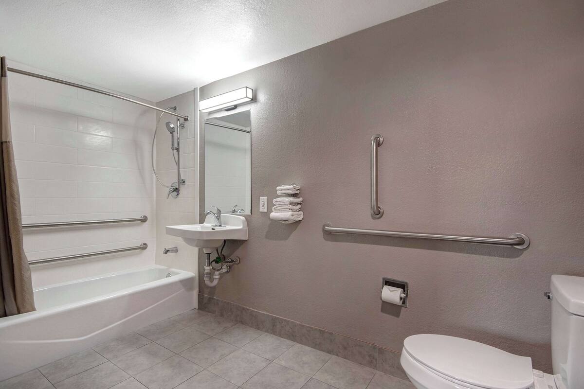 Un bagno con vasca, lavandino, WC e mancorrenti.