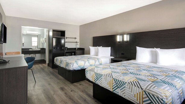 Ein Hotelzimmer mit zwei Betten, einem Schreibtisch, einem Stuhl, einem Spiegel und einem Badezimmer.