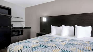 A hotel room with a bed, a nightstand, a microwave, and a small kitchenette.