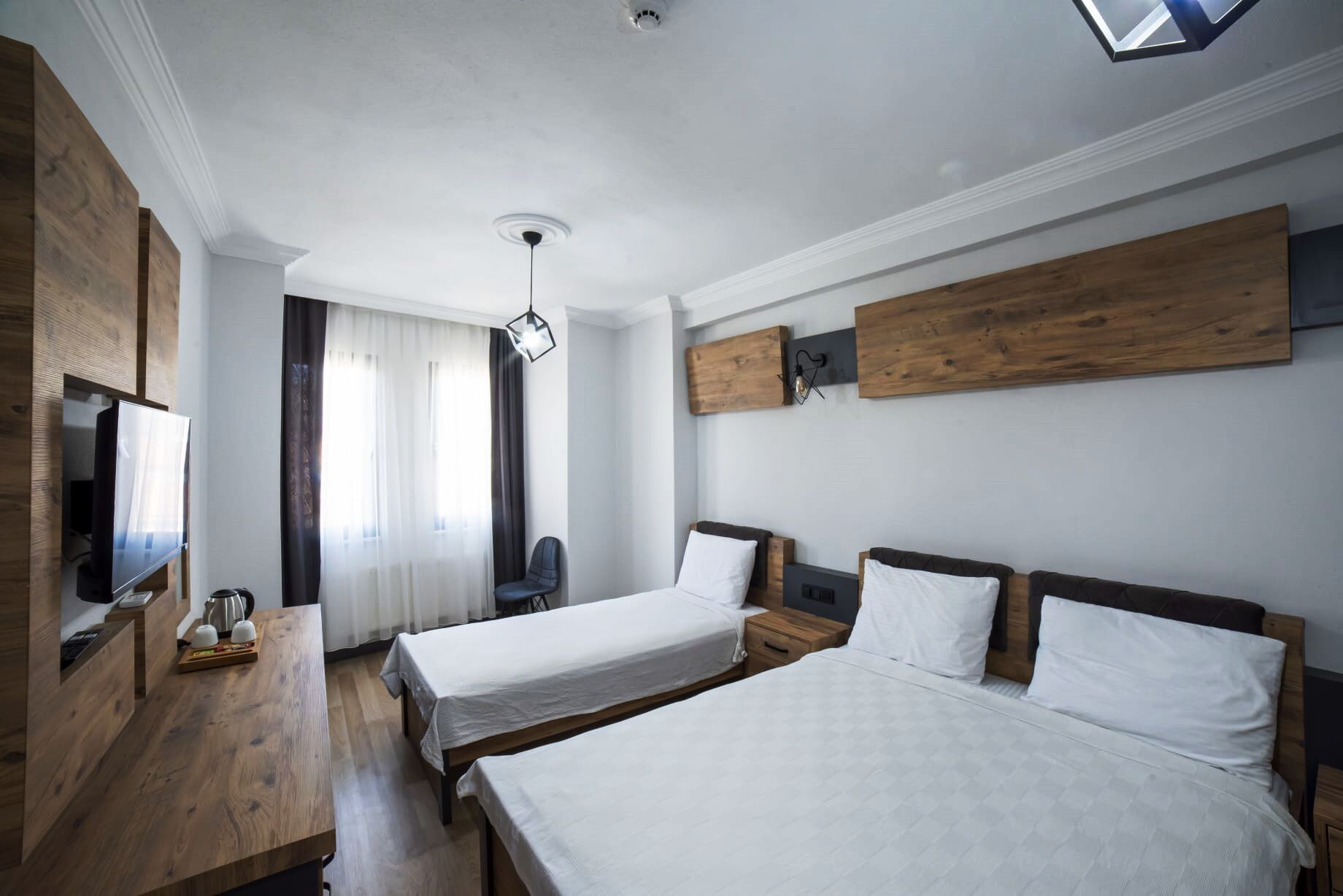 A hotel room with two beds, a wooden desk, a TV, and a ceiling light.
