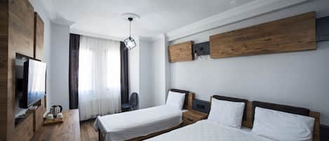 A hotel room with two beds, a wooden desk, a TV, and a ceiling light.