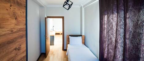 A narrow hallway leading to a bed with a wooden headboard and white bedding. A modern pendant light hangs from the ceiling.