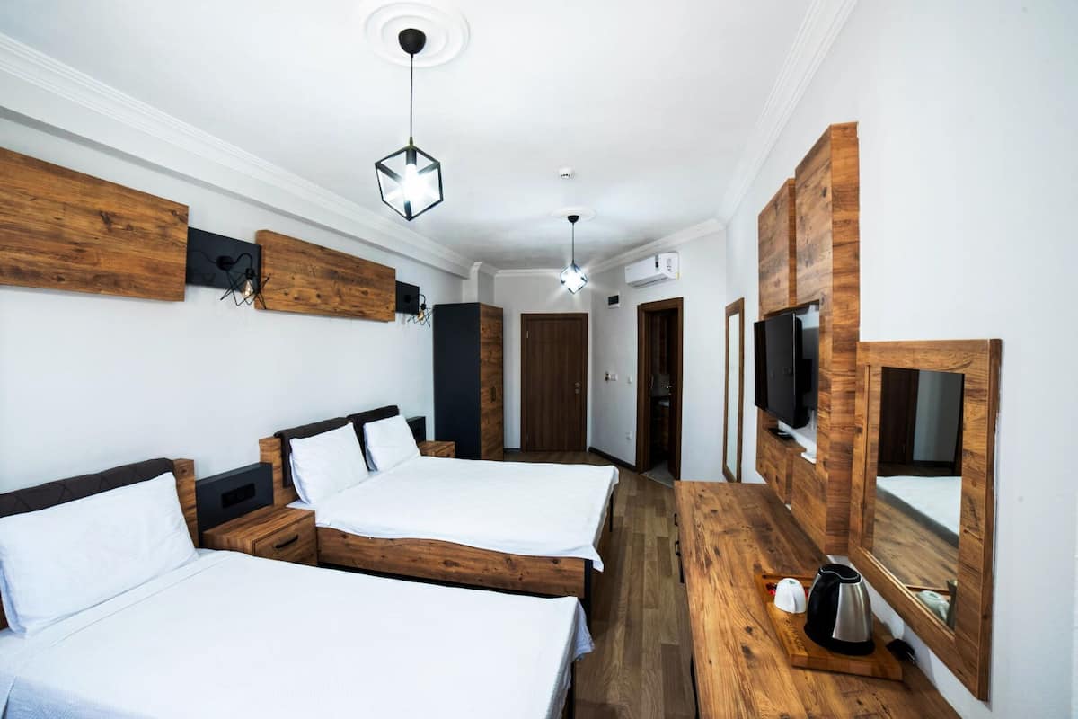 A hotel room with two beds, wooden headboards, a flat-screen TV, a coffee maker, and a wooden sideboard.
