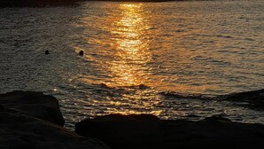 Atardecer sobre una zona costera con formaciones rocosas y agua tranquila que refleja la luz del sol.