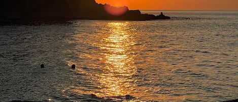 Atardecer sobre una zona costera con formaciones rocosas y agua tranquila que refleja la luz del sol.