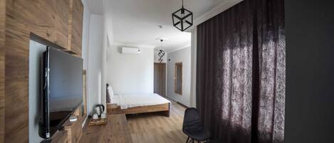 A modern bedroom with a wooden wall, a large bed, a TV, and a dining area.