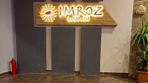 Un vestíbulo de hotel con piso de baldosas pulidas, un letrero de neón para IMROZ butikotel y un extintor cerca de la entrada.