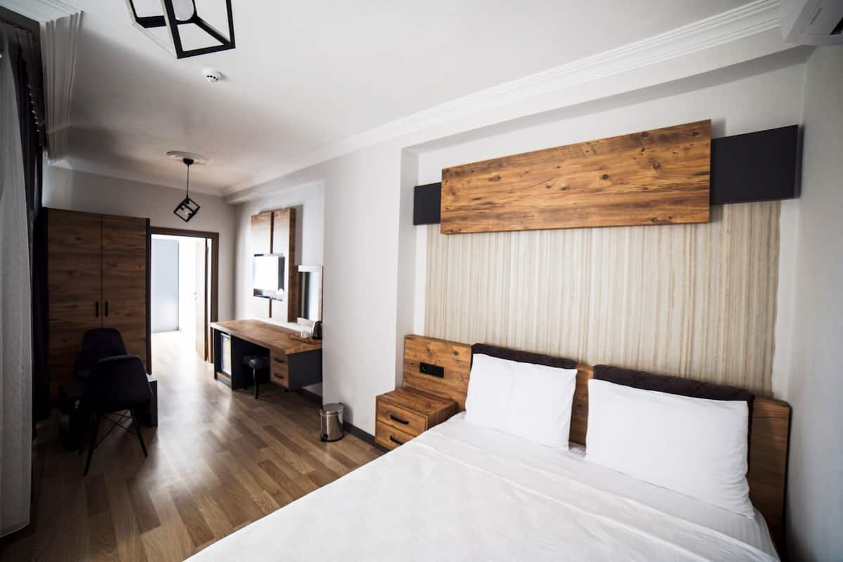 A modern bedroom with a wooden headboard, a large bed, a desk, and a wardrobe.