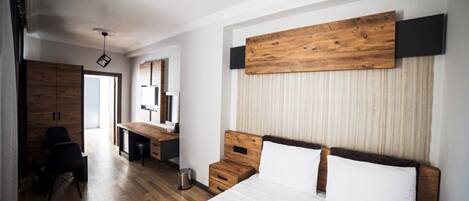 A modern bedroom with a wooden headboard, a large bed, a desk, and a wardrobe.