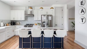 A modern kitchen with white cabinets, a central island with bar stools, stainless steel appliances, and pendant lighting. - Three Story Home With Urban Courtyard Minutes to Downtown (Nashville)