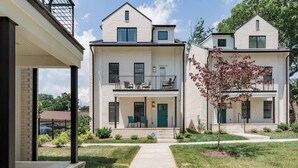 A two-story residential building with a covered front porch, a small balcony on the upper floor, and a well-maintained lawn. - Three Story Home With Urban Courtyard Minutes to Downtown (Nashville)