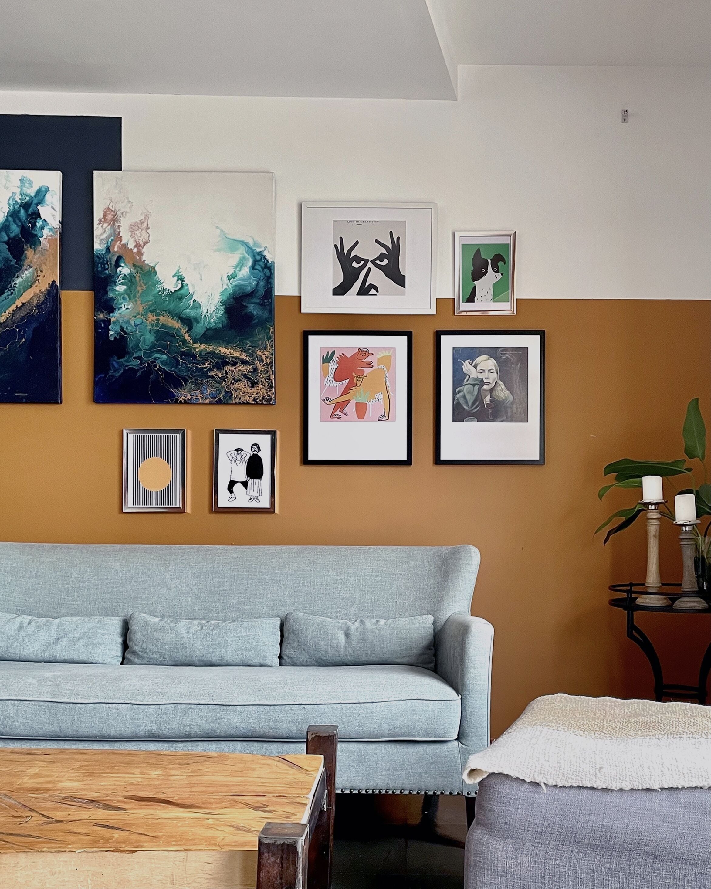 A living room with a light blue sofa, a wooden coffee table, and various framed artworks on the wall.