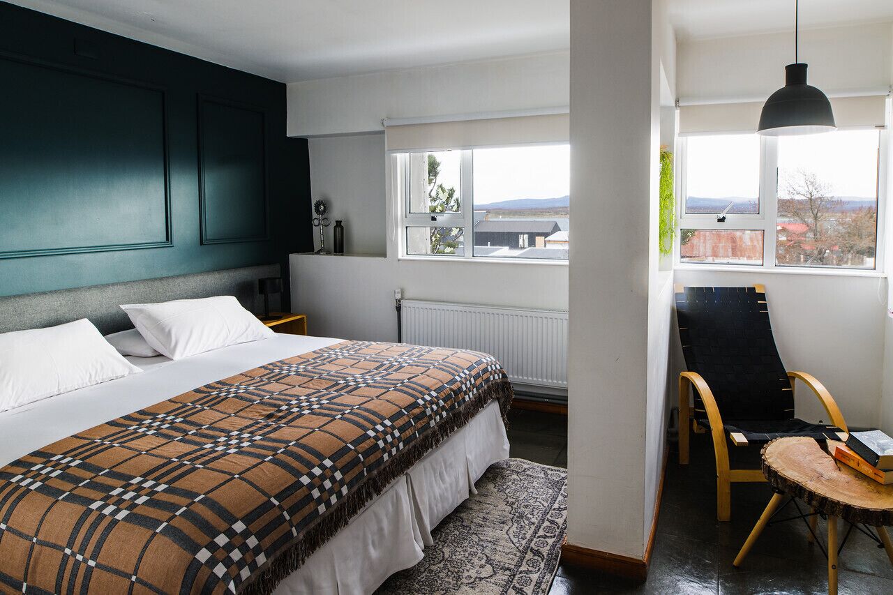 A bedroom with a large bed, a window with a view, a chair, and a hanging light fixture.