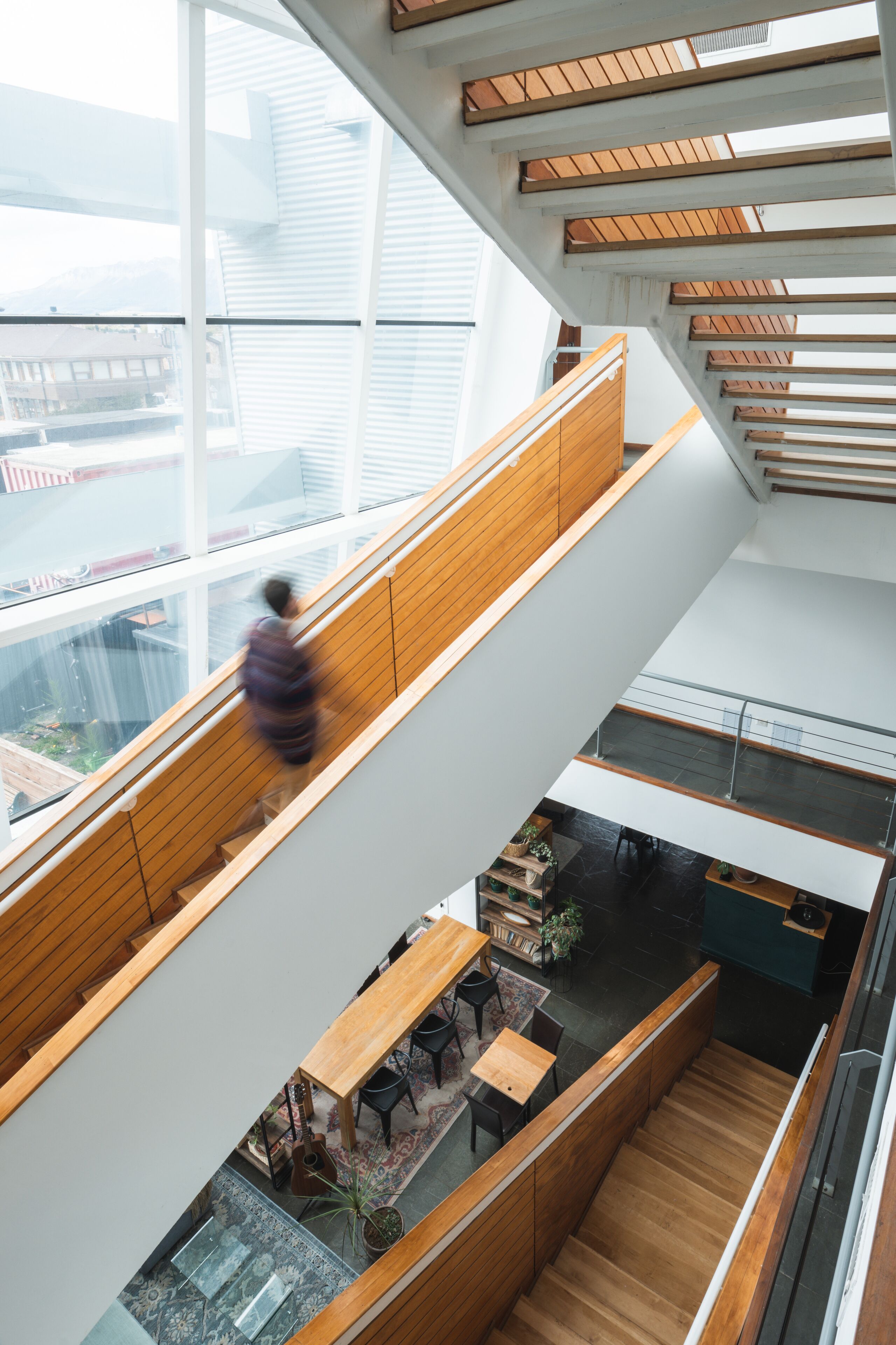Un intérieur à plusieurs niveaux, doté de rampes en bois, d’un escalier et d’un coin repas avec des tables et des chaises.